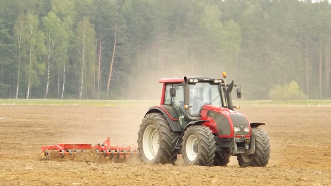 Sarkans traktors apstrādā lauku. 