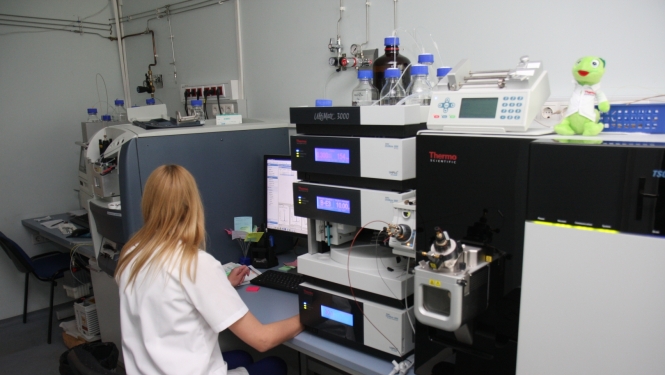 Laboratorijas darbinieks sēž pie datora un strādā ar analītiskām iekārtām. 