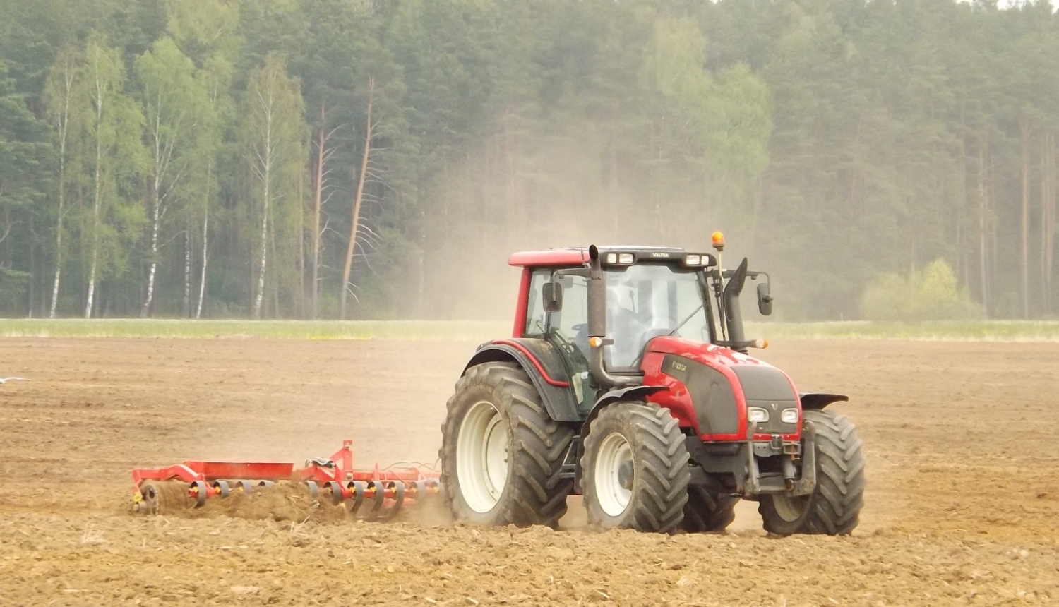 Sarkans traktors apstrādā lauku. 