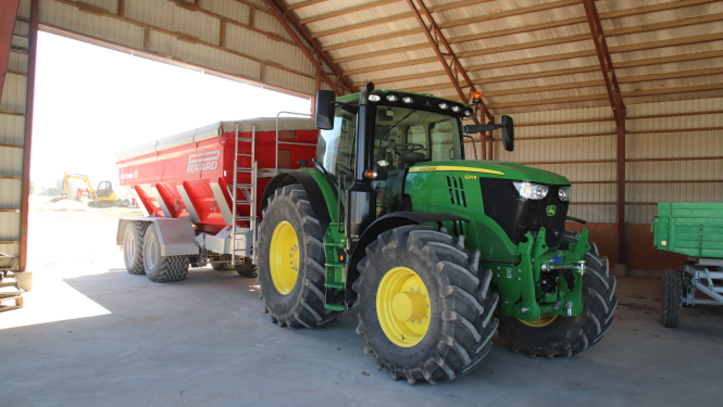 Jauns John Deere traktors ar piekabi angārā