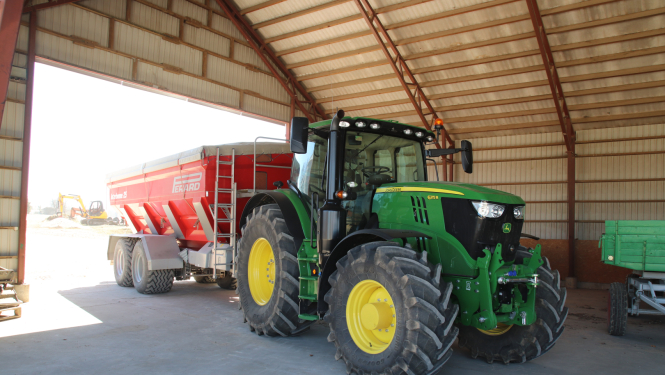 Jauns John Deere traktors ar piekabi angārā