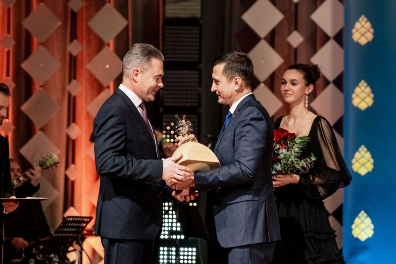 Zemkopības ministrs Armands Krauze pasniedz balvu vīirietim, uz skatuves arī meitene ar sarkaniem ziediem rokās