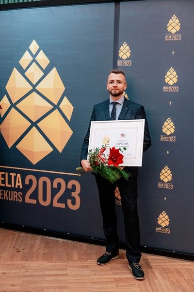 Pie zilas ar zelta čiekuriem foto sienas vīrietis, kas tur rokās diplomu un sarkanus ziedus