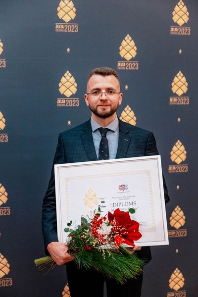 Pie zilas ar zelta čiekuriem foto sienas vīrietis, kas tur rokās diplomu un sarkanus ziedus