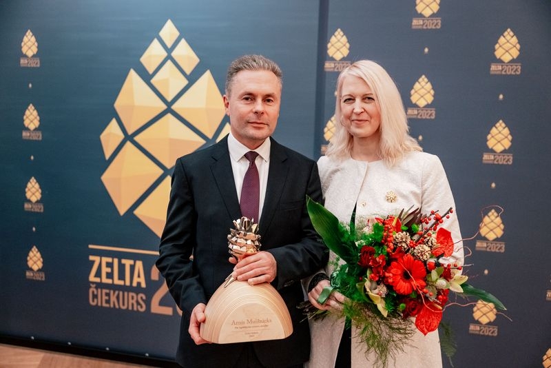 Pie zilas ar zelta čiekuriem foto sienas vīrietis, kas tur rokās diplomu un sieviete kas tur rokās sarkanus ziedus