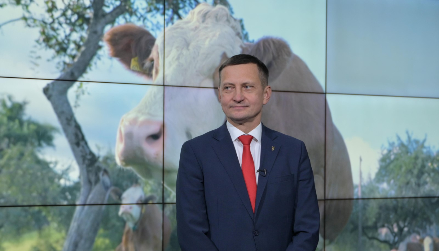zemkopības ministrs Armands Krauze, fonā uz ekrāna lauku aiva ar govīm