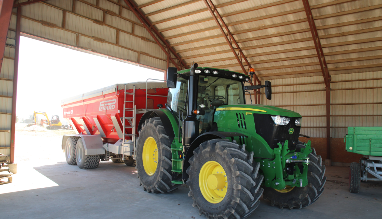 Jauns John Deere traktors ar piekabi angārā