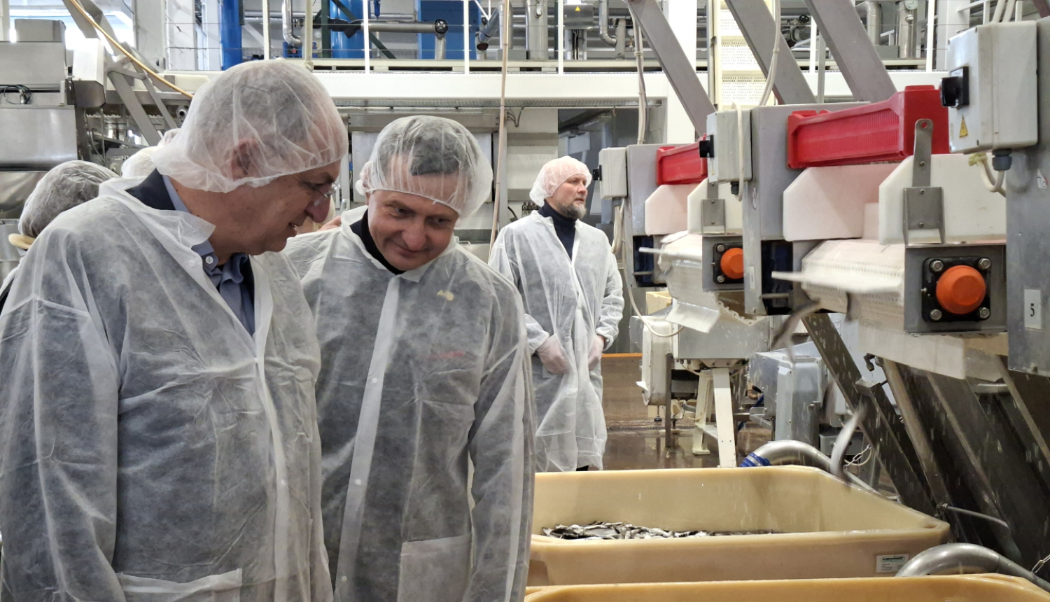 vairāki vīrieši baltos aizsargtērpos zivju pārstādes uzņēmumā