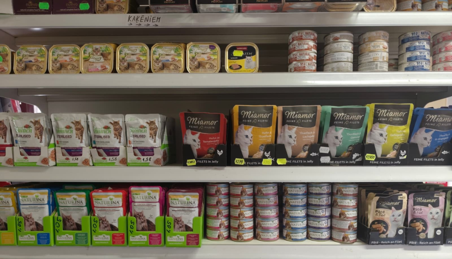 Kaķu barības sortiments veikala plauktos, piedāvājot dažādu zīmolu un veidu produktus mājdzīvnieku uzturam.