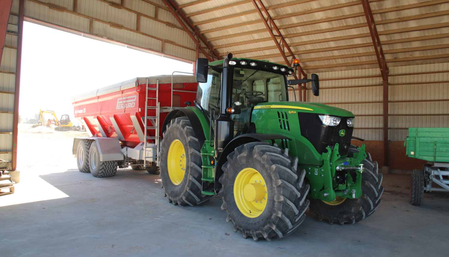 Jauns John Deere traktors ar piekabi angārā